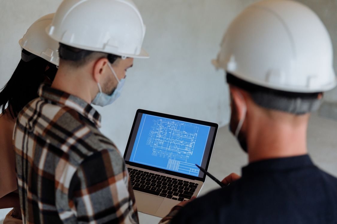 Equipe de engenheiros analisa documentos técnicos em laptop